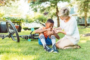 A mother tends to her son's scraped knee after a bicycle fall on a sunny day in the park.