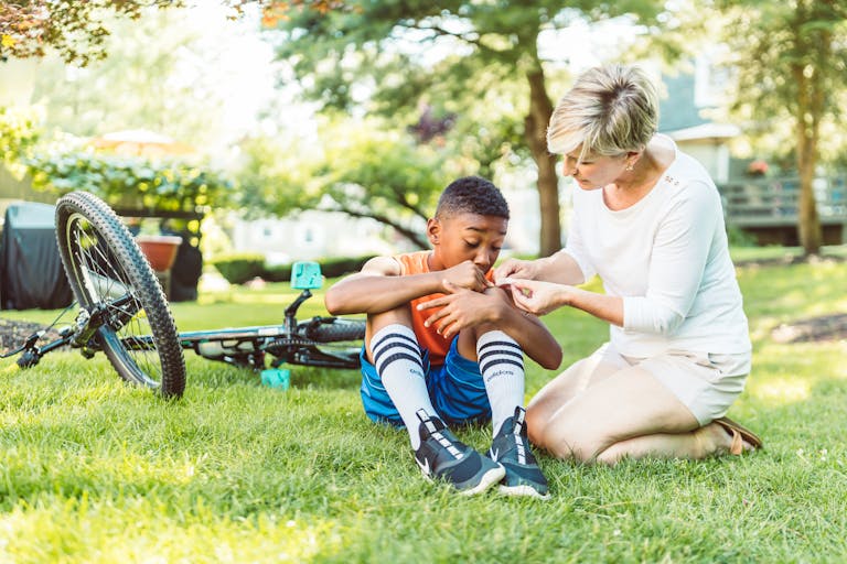 A mother tends to her son's scraped knee after a bicycle fall on a sunny day in the park.